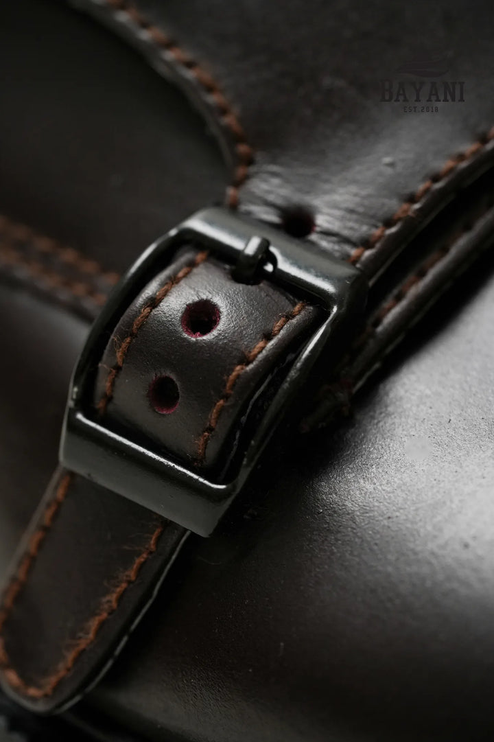 Close-up of a brown leather strap with a black buckle on a dark background
