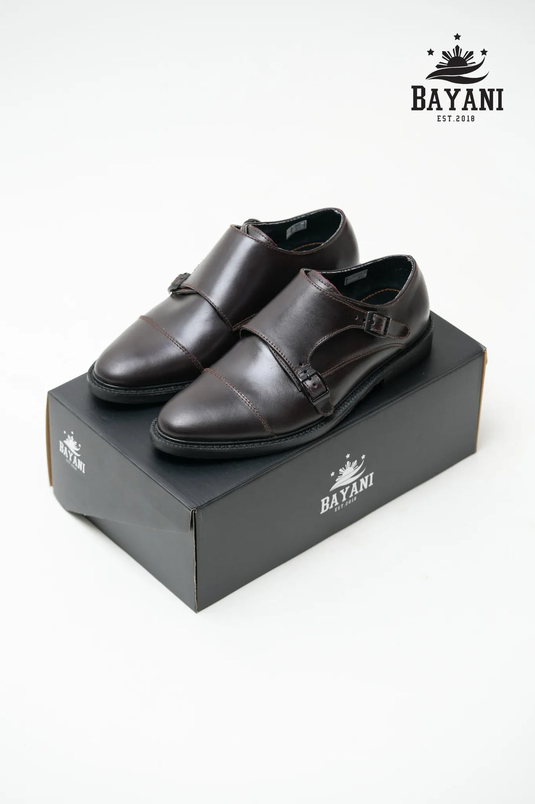 Pair of black dress shoes on a Bayani branded box with the Bayani logo above.
