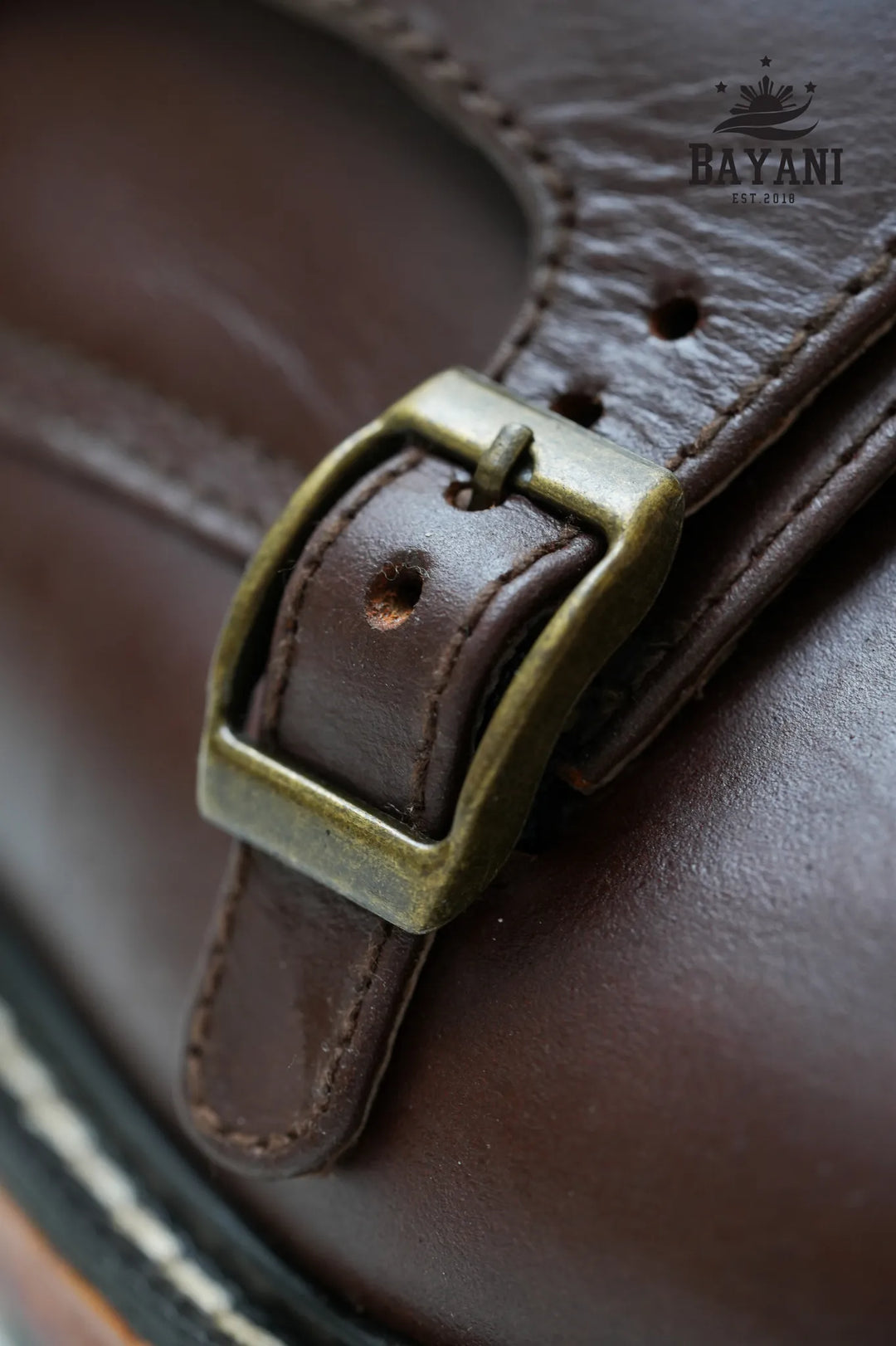 Close-up of a brown leather strap with a brass buckle on a product, branded &