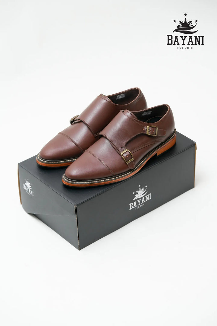 Brown monk strap shoes on a Bayani branded box with the Bayani logo above.
