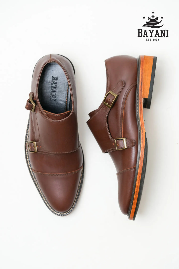 Brown leather shoes with gold buckles on a white background, featuring the Bayani brand logo.
