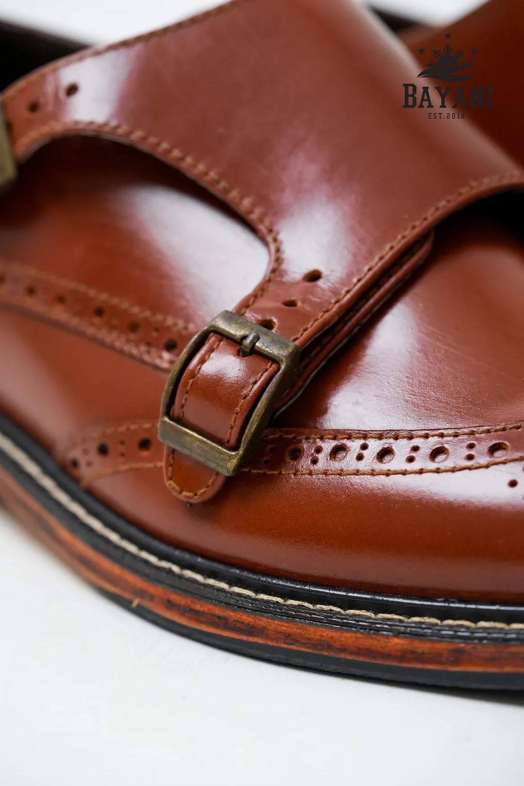 Brown leather sandal with a buckle on a white background, featuring the BAYANI brand.
