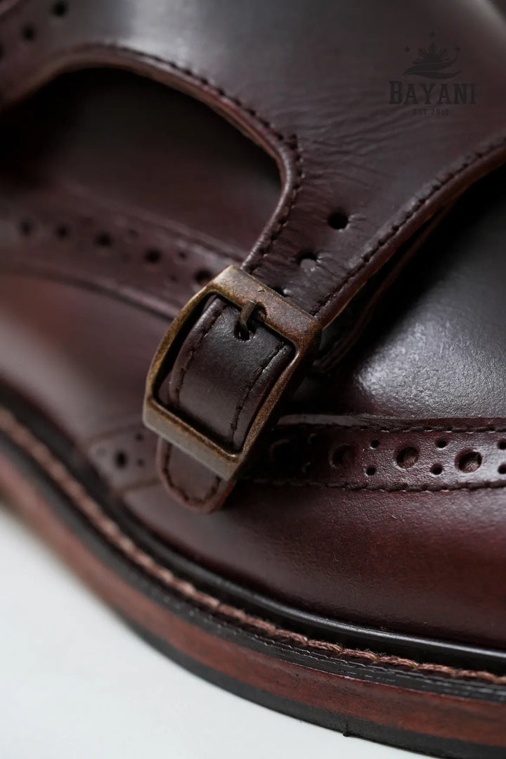 Close-up of a brown leather sandal with a strap and buckle, featuring the brand &
