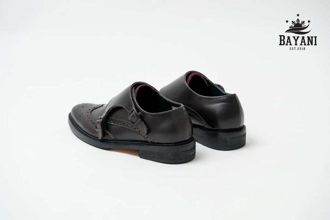 Pair of black shoes with a strap on a white background, featuring the Bayani brand logo.
