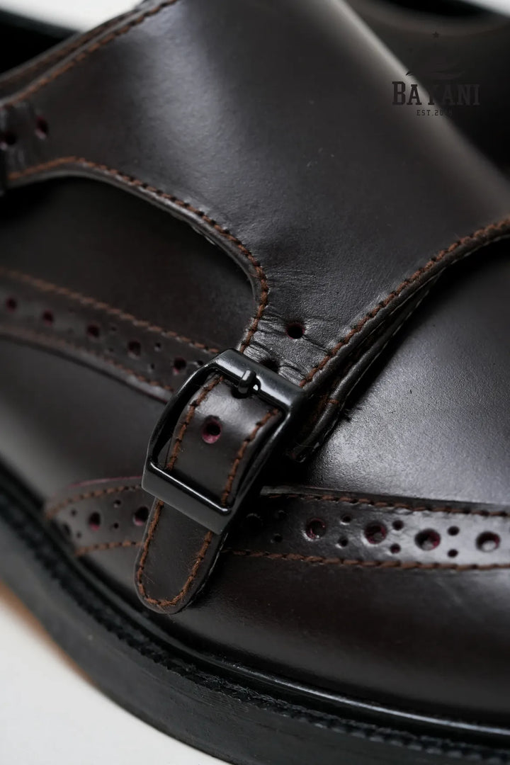 Close-up of a brown leather sandal with a strap and buckle, featuring the brand &