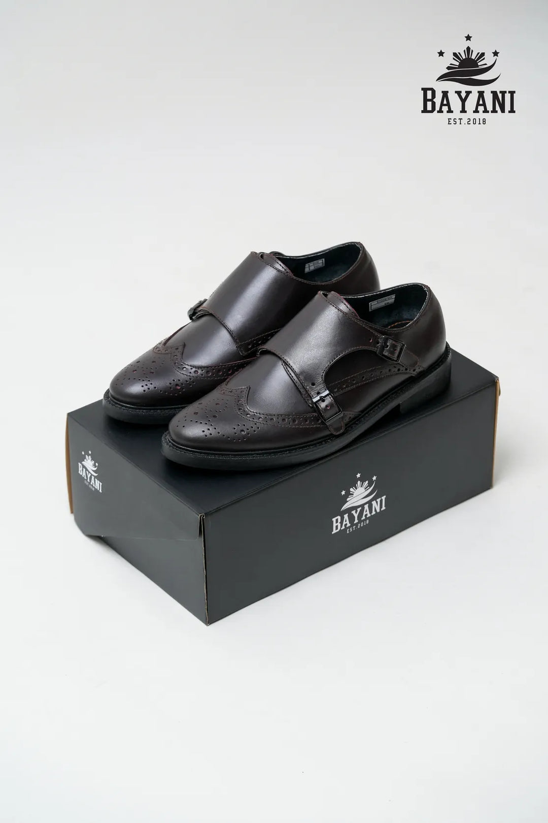 Black dress shoes on a Bayani branded box with the Bayani logo above.
