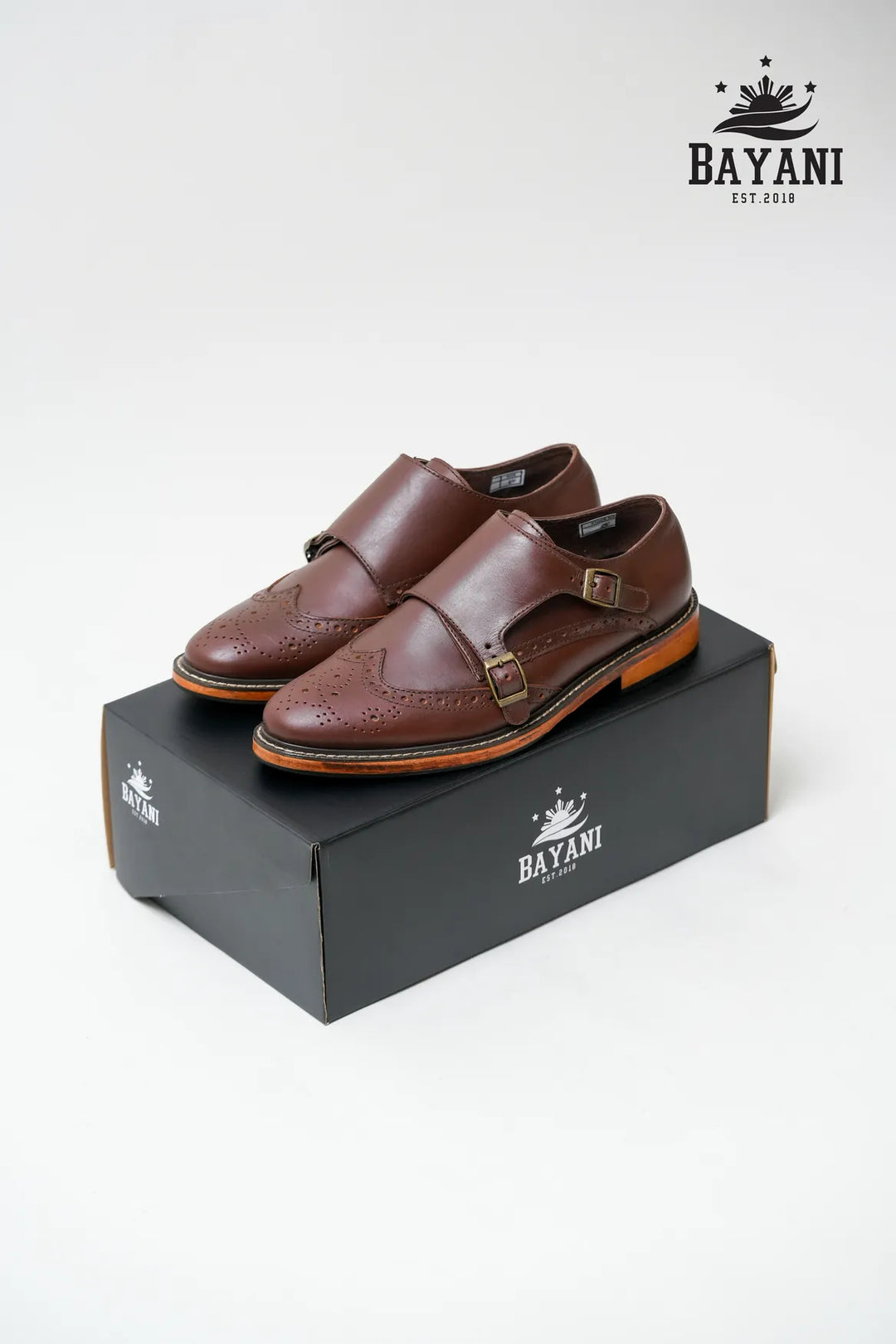 Brown leather shoes on a black box with Bayani logo above, on a white background
