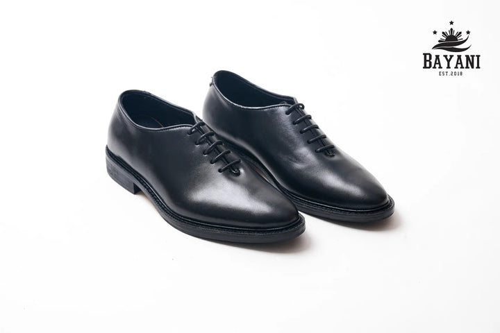 Pair of black leather shoes on a white background with Bayani logo.
