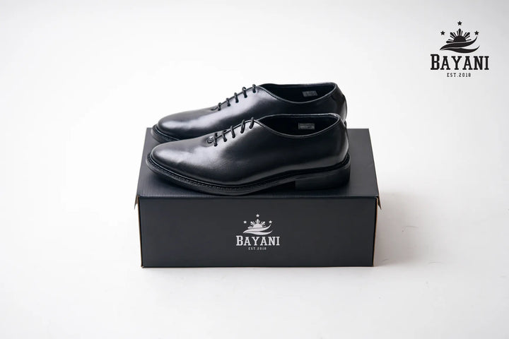 Black dress shoes on a black box with Bayani logo on a white background
