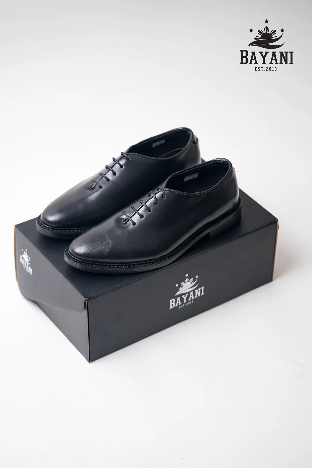 Black dress shoes on a black Bayani box with the brand logo.
