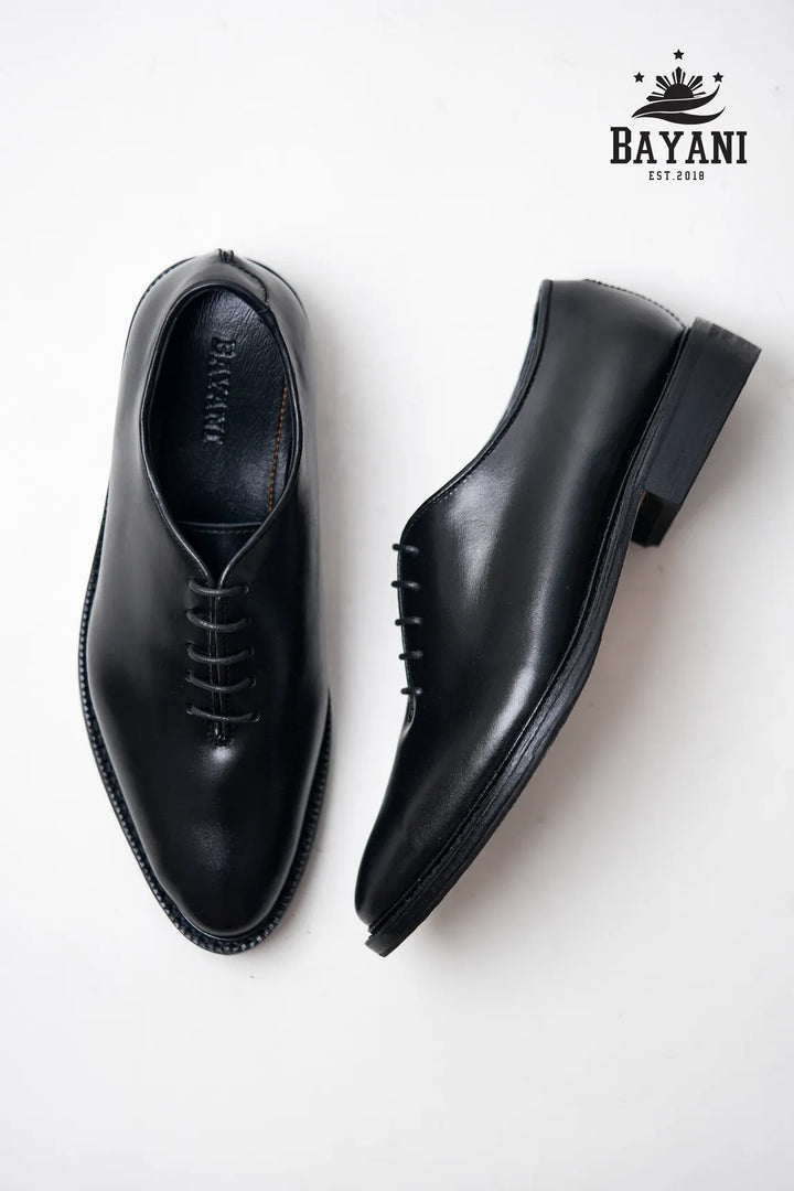 Pair of black dress shoes on a white background with Bayani logo.
