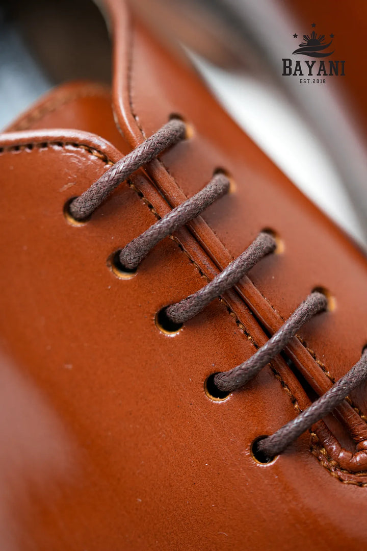 Close-up of a brown leather shoe with laces, featuring the Bayani brand logo.
