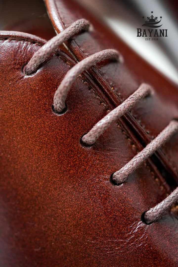 Close-up of a brown leather shoe with visible stitching, featuring the Bayani logo.
