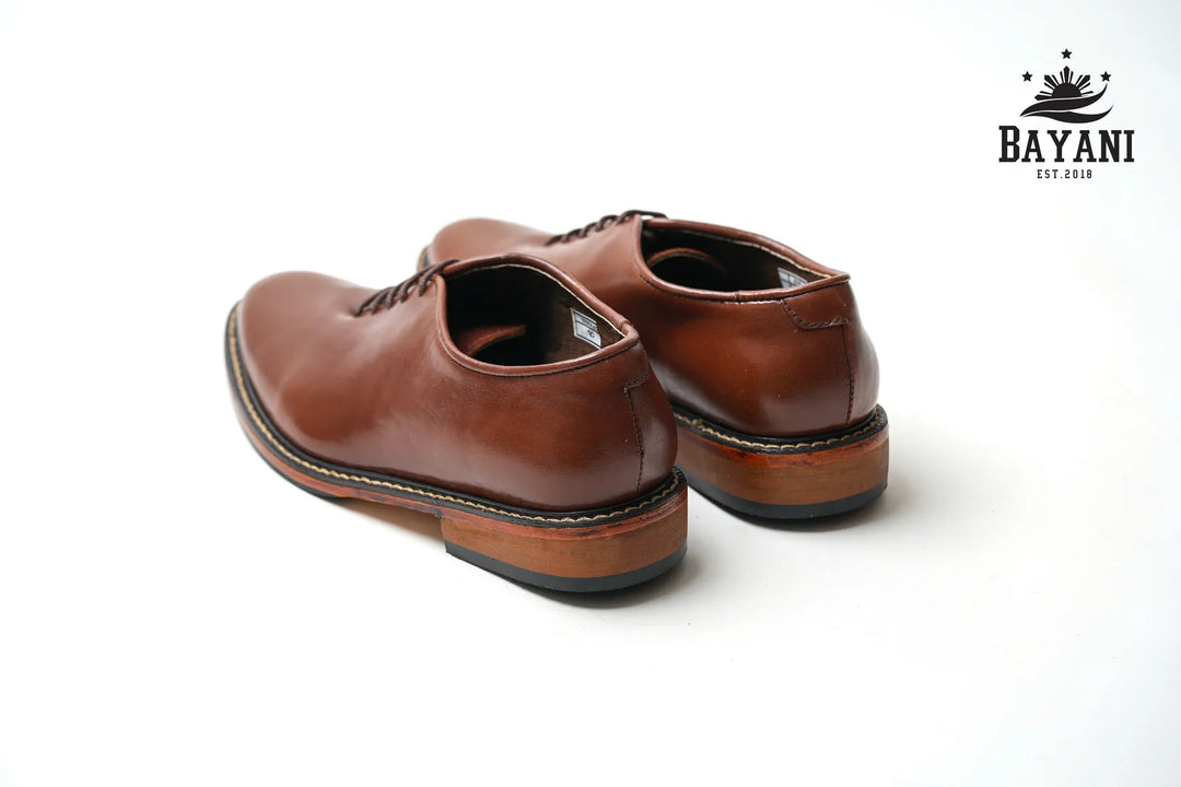 Pair of brown leather shoes on a white background with Bayani logo.
