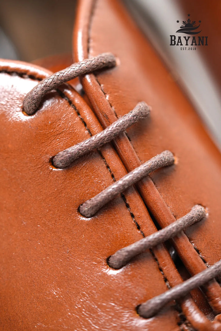 Close-up of a brown leather shoe with laces, featuring the Bayani brand logo.

