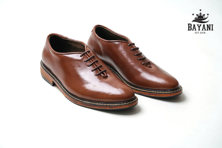 Pair of brown leather shoes on a white background with Bayani logo.
