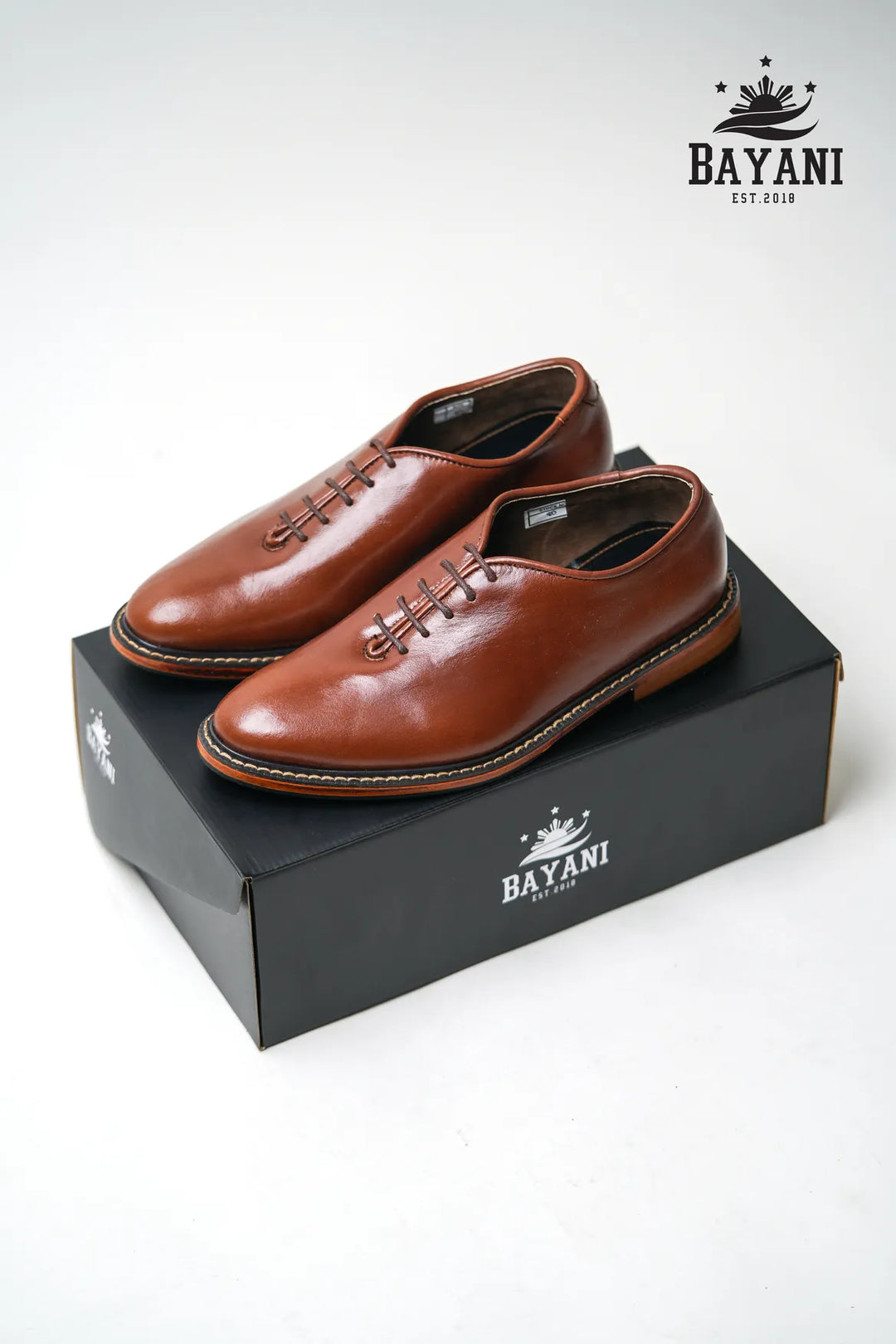 Brown leather shoes on a black Bayani box with the brand logo.
