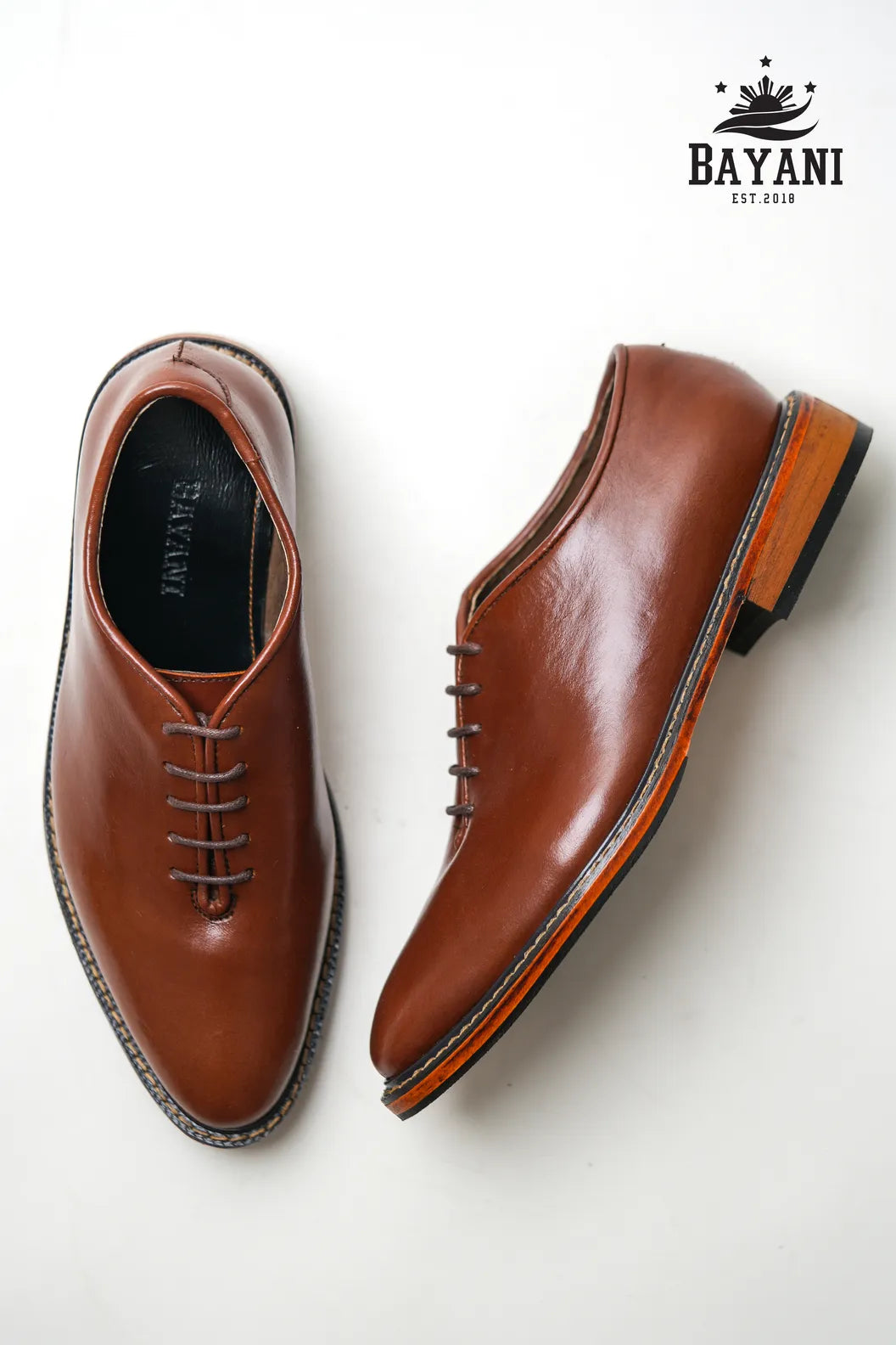 Brown leather shoes on a white background with Bayani logo.
