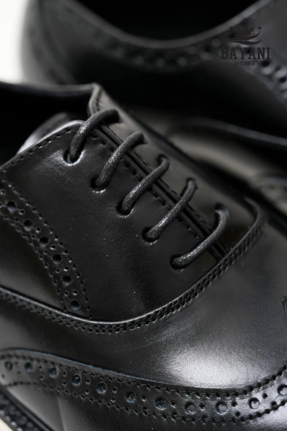 Close-up of black leather dress shoes with detailed sole design, brand 'Bayani' visible.
#color_black