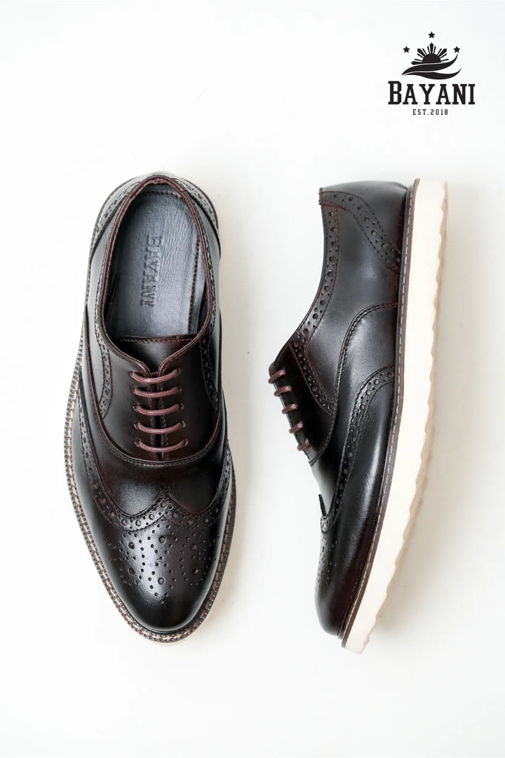 Pair of black leather brogue shoes on a white background with Bayani logo.
