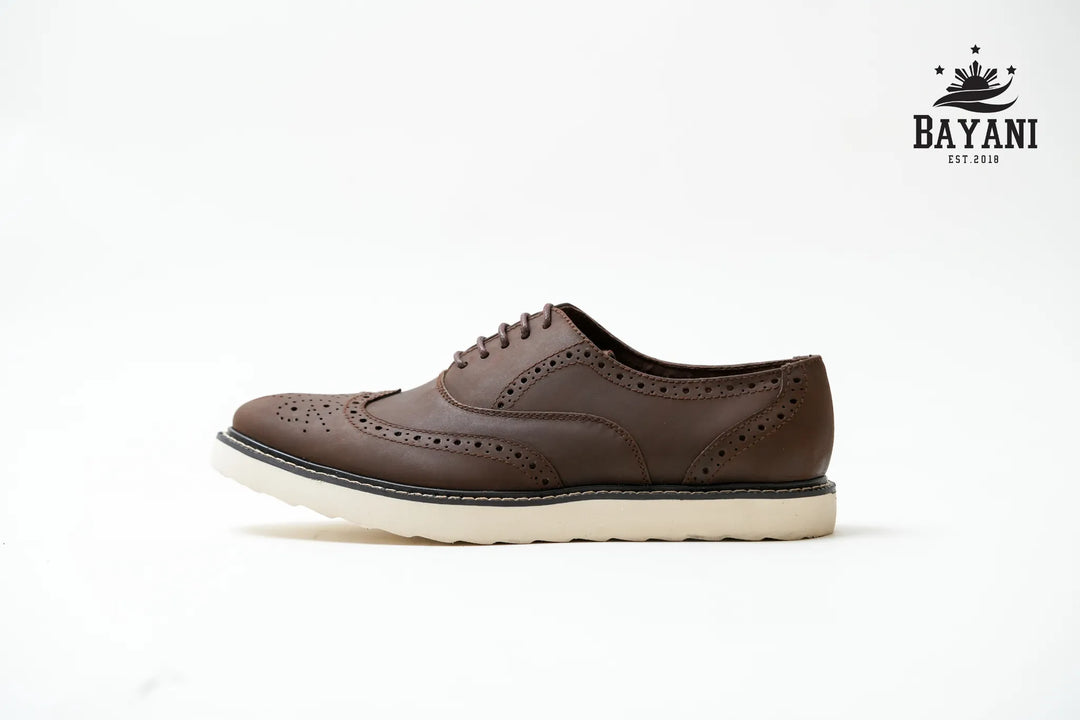 Brown leather shoe with white sole on a light gray background, featuring the Bayani brand logo.
