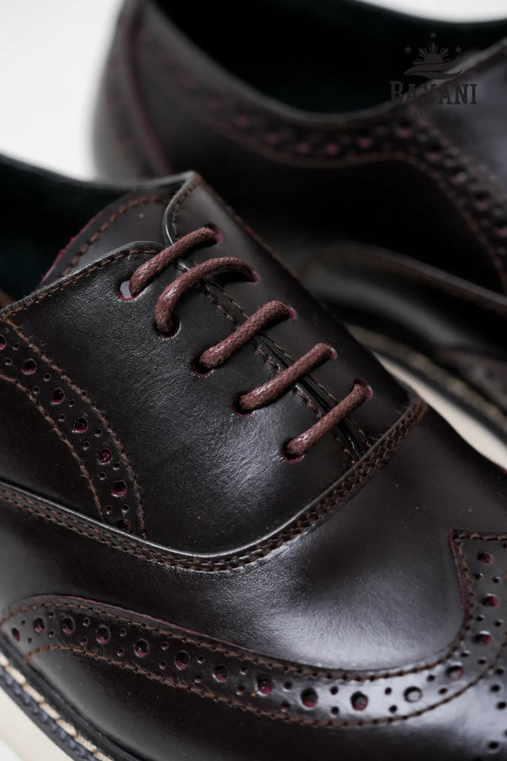 Close-up of dark brown leather dress shoes with brogue detailing on a white background.
