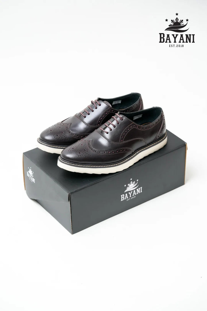 Brown leather shoes with white soles on a Bayani branded box against a white background
