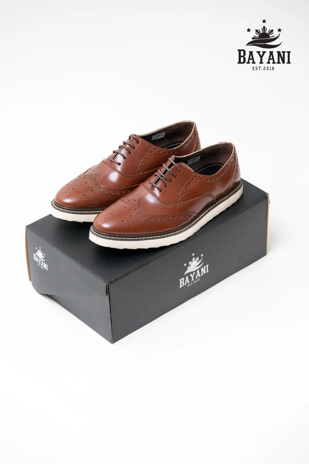 Brown leather shoes on a black box with Bayani logo above.

