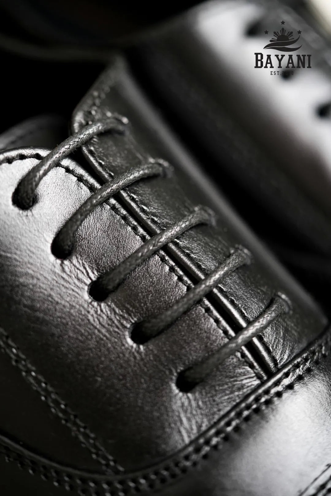 Close-up of a black leather shoe with laces, featuring the Bayani logo.
