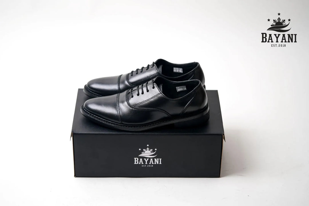 Black dress shoes on a black box with Bayani logo against a white background
