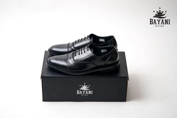 Black dress shoes on a black box with Bayani logo against a white background
