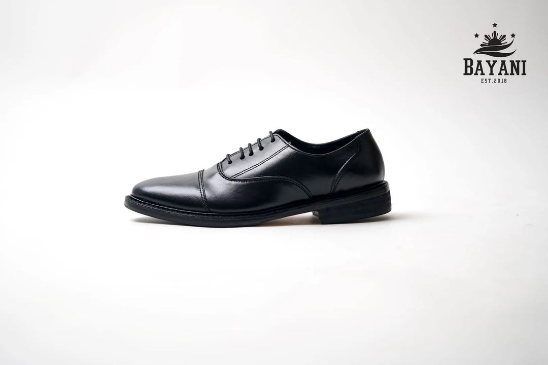 Black dress shoe on a white background with Bayani logo.
