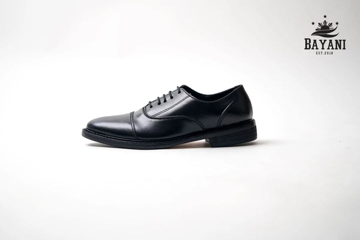 Black dress shoe on a white background with Bayani logo.
