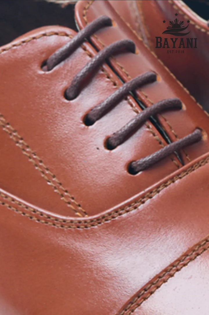 Close-up of a brown leather shoe with laces, featuring the Bayani logo.
