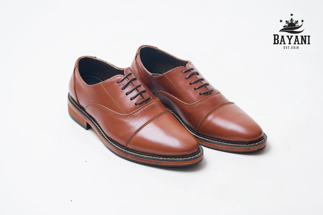 Brown leather shoes with black laces on a white background, featuring the Bayani logo.

