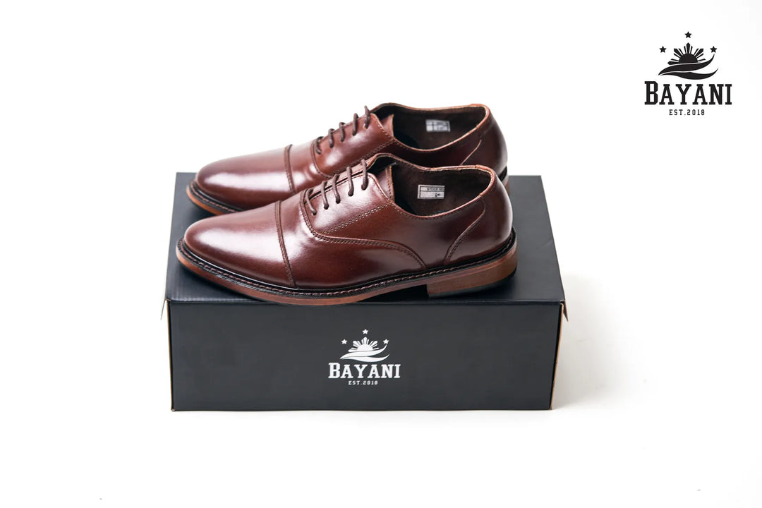 Brown dress shoes on a black Bayani branded box with the brand logo.
