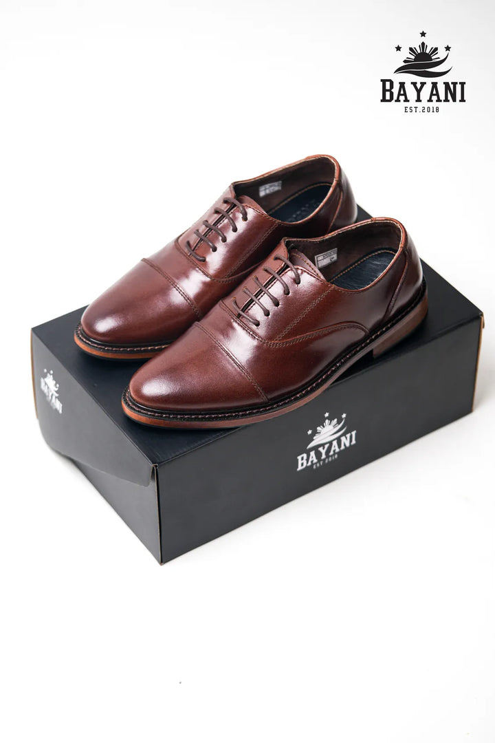 Brown leather shoes on a black box with Bayani logo, on a white background

