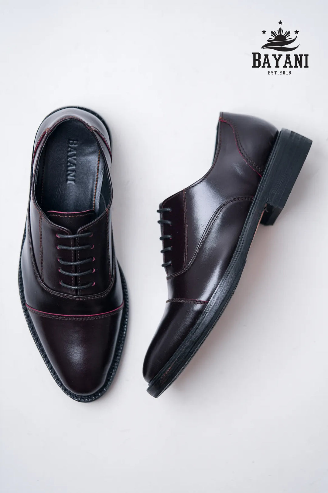 Pair of black dress shoes on a white background with Bayani logo.
