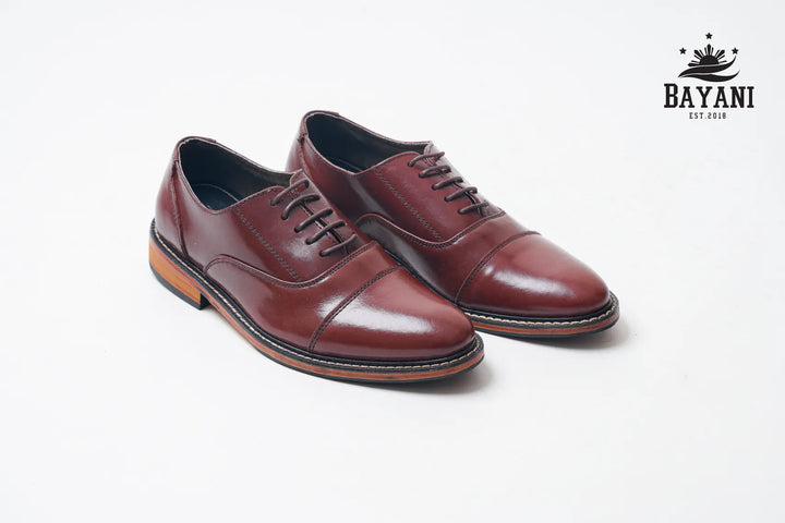 Pair of brown leather shoes on a white background with Bayani logo.
