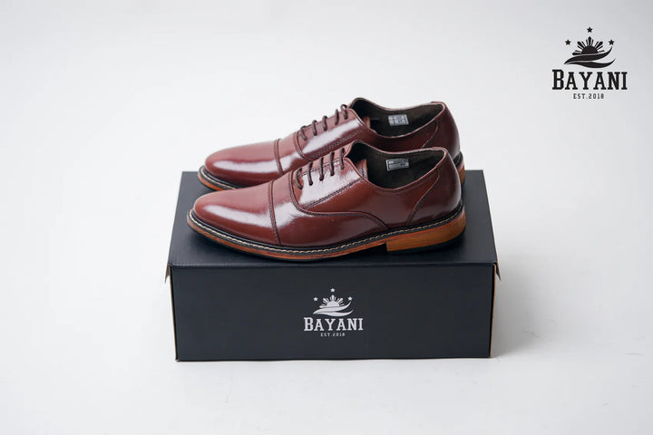 Brown leather shoes on a black box with Bayani logo, on a white background
