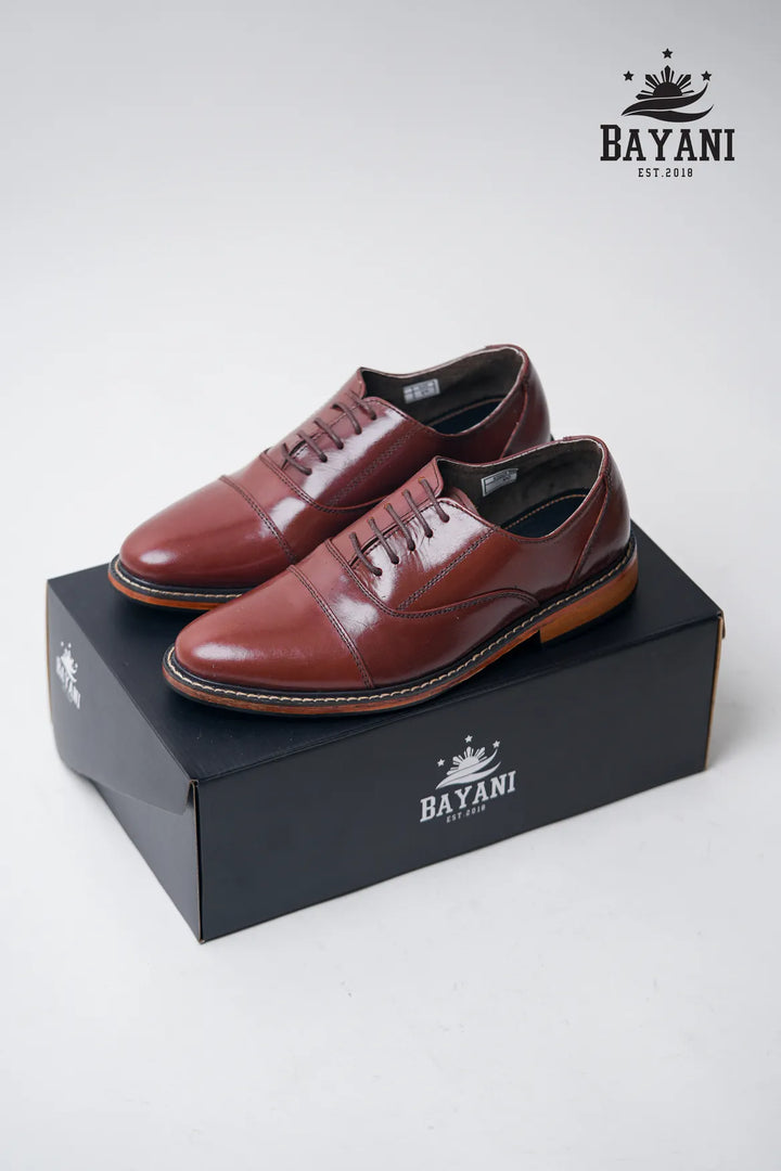 Brown leather shoes on a black box with Bayani logo, on a white background
