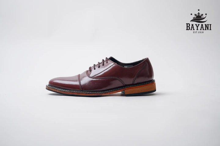 Brown leather dress shoe on a light gray background with Bayani logo.
