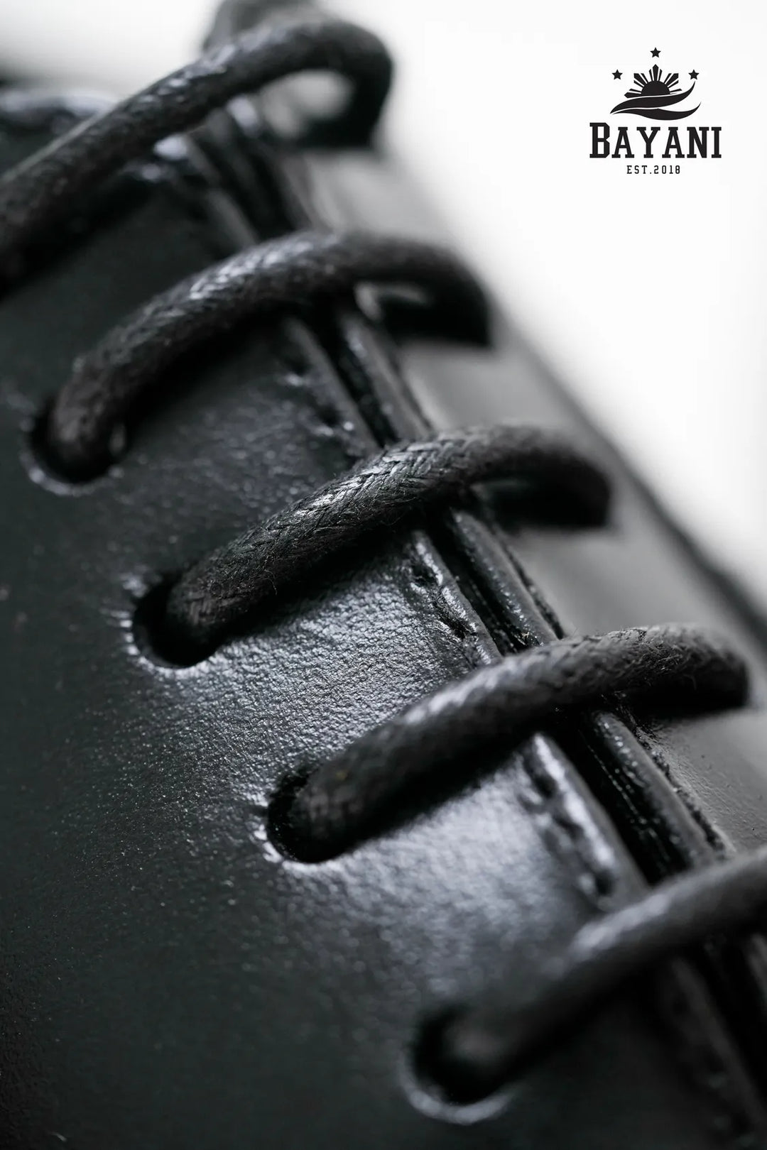 Close-up of black leather shoe with laces, featuring Bayani logo.
