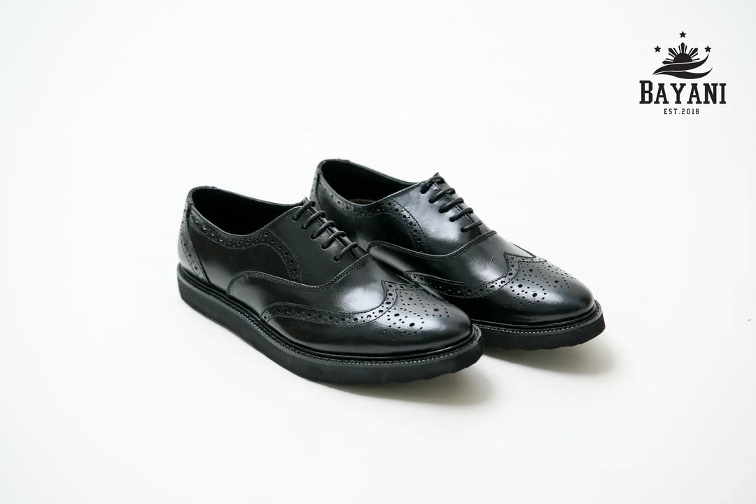 Pair of black leather shoes on a white background with Bayani logo.
