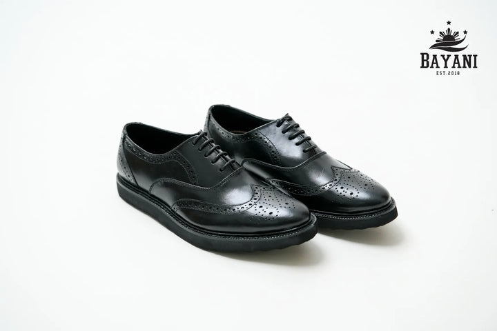 Pair of black leather shoes on a white background with Bayani logo.

