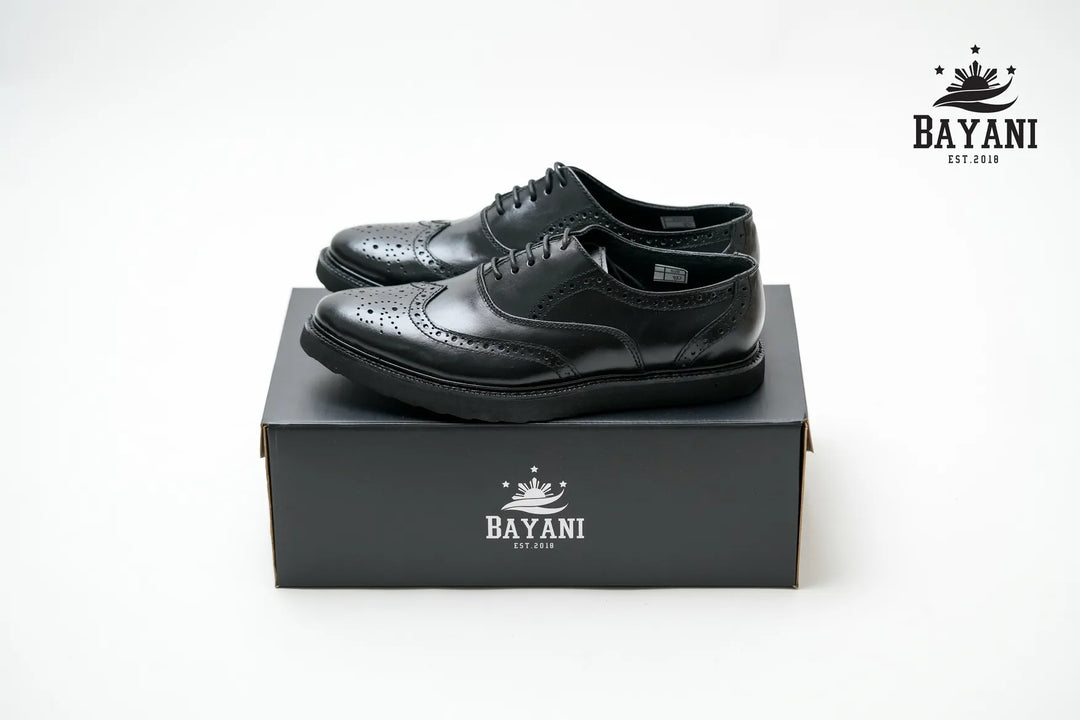 Black leather shoes on a Bayani branded box with the Bayani logo above.
