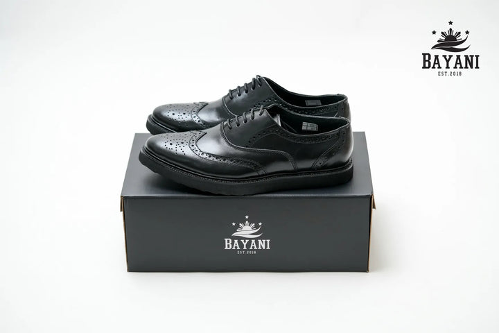 Black leather shoes on a Bayani branded box with the Bayani logo above.
