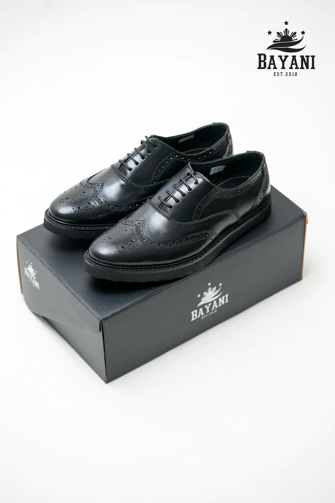 Black dress shoes on a Bayani branded box with the Bayani logo above.
