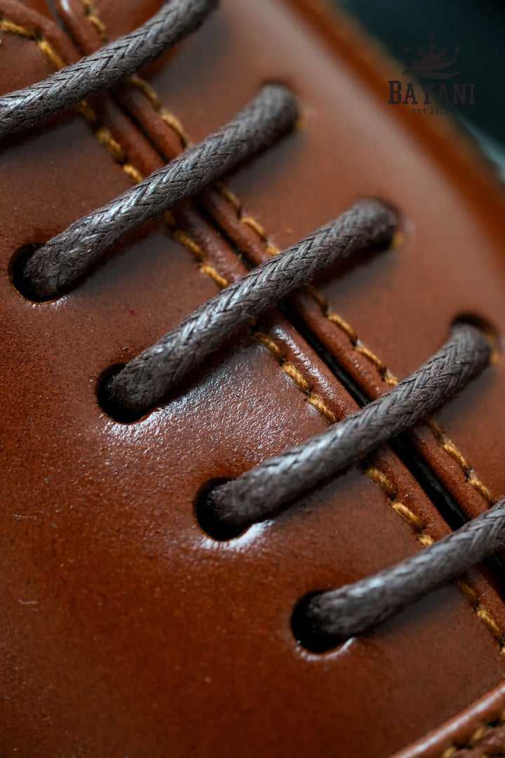 Close-up of brown leather shoe with black laces and Bayani brand logo.
