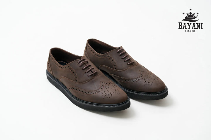 Pair of brown leather shoes on a white background with Bayani logo.
